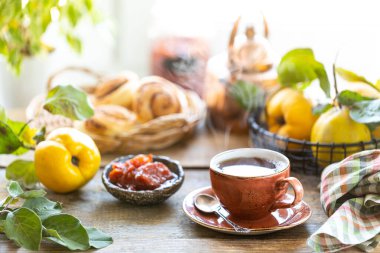 Eski ahşap arka planda ev yapımı ayva reçeli bir fincan çay. Arka planda taze meyve ve ayva yaprakları var. Yatay fotoğraf. kırsal