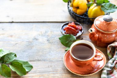 Eski ahşap arka planda ev yapımı ayva reçeli bir fincan çay. Arka planda taze meyve ve ayva yaprakları var. Yatay fotoğraf. Uzayı kopyala Mesaj için yer. Üst görünüm
