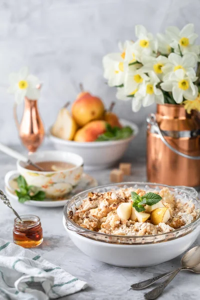 Запечённая груша крошится с грушами и медом в белом блюде на столе с медной посудой и цветами — стоковое фото