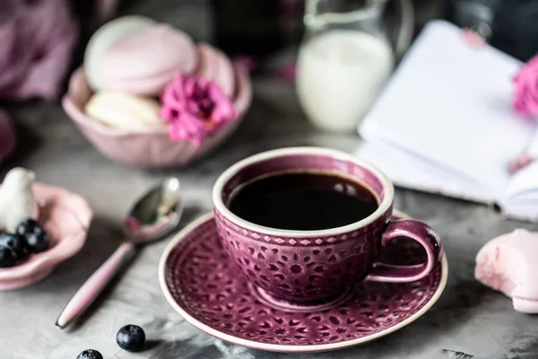 Filiżanka kawy na śniadanie z piankami w postaci ciastek makaronowych w czarnej misce na ciemnym stole i z kwiatami w szklance — Zdjęcie stockowe