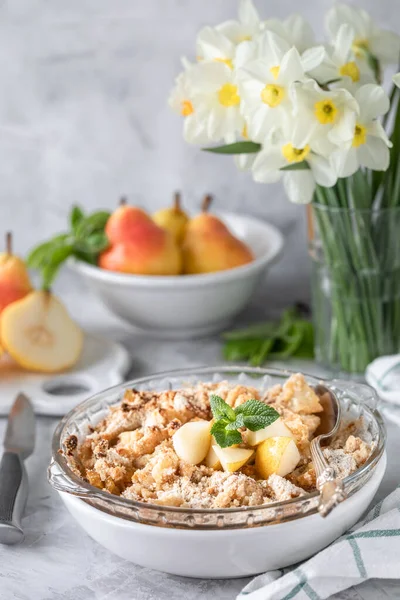 Baked pear crumble with pears and honey in a white dish on the table with copper utensils and flowers — Stock Photo, Image