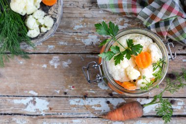 Eski ahşap bir masada cam bir kavanozda havuçlu karnabahar turşusu. Mayalanmış yiyecek. Uzayı kopyala en üstteki görünüm