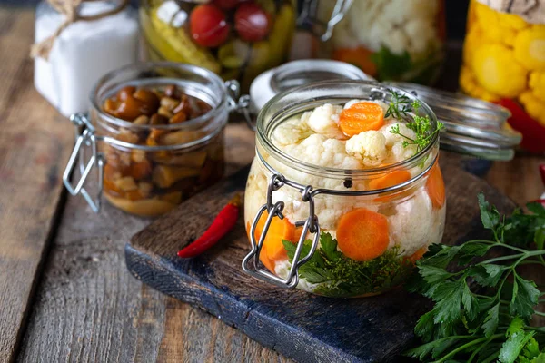 Ingelegde bloemkool met wortelen in een glazen pot op een donkere houten tafel. Gefermenteerd voedsel. — Stockfoto
