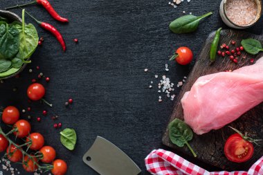 Çiğ hindi filetosu ızgara için hazır. Çeri domatesli, acı biberli, ıspanak yapraklı ve yeşillikli ahşap kesme tahtasındaki tavuk filetosu. kopyalama alanı. en üstteki görünüm