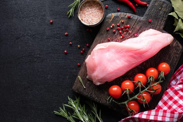 Raw turkey fillet ready for grilling. Chicken fillet on a wooden cutting board with cherry tomatoes, hot pepper, spinach leaves and greens. copy space. top view