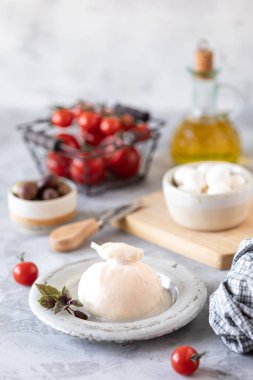 İtalyan peynirli burrata ve zeytin ve kiraz domatesli mozzarella açık arkaplanda yuvarlak beyaz bir tabakta.