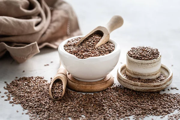 Flax seeds in a ceramic bowl with a wooden spoon on a white background. Organic healthy food. — Stock Photo, Image