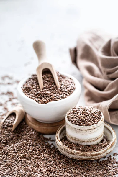 Flax seeds in a ceramic bowl with a wooden spoon on a white background. Organic healthy food. Vertical photo — Stock Photo, Image