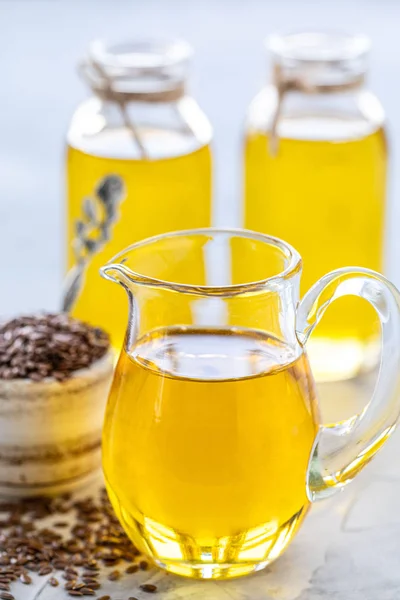 Flaxseed oil in a bottle and ceramic bowl with brown flax seeds and wooden spoon on a white background. vertical — Stock Photo, Image