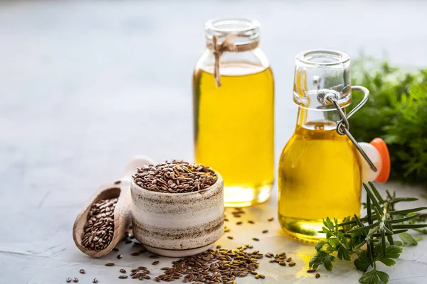 Flaxseed oil in a bottle and ceramic bowl with brown flax seeds and wooden spoon on a white background — Stock Photo, Image