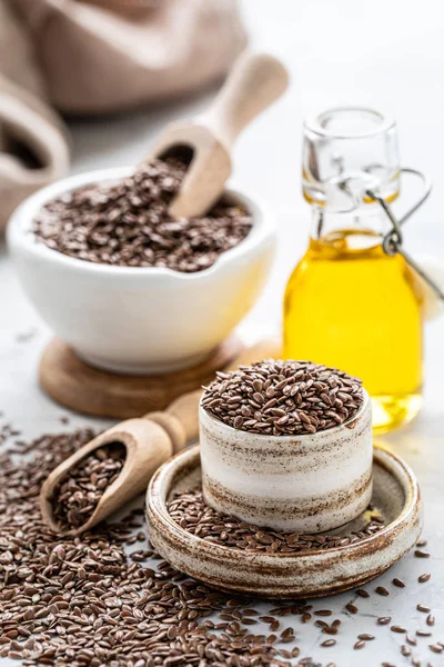 Flaxseed oil in a bottle and ceramic bowl with brown flax seeds and wooden spoon on a white background. vertical — Stock Photo, Image