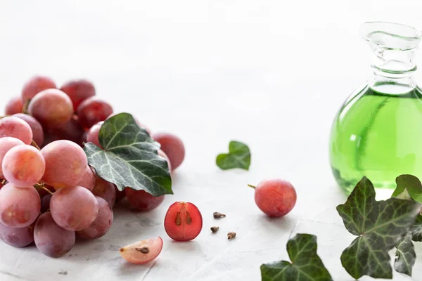 Grape seed oil in a glass bottle with a bunch of grapes on a white background. Place for text