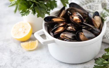 Beton arka planda beyaz bir tavada taze otlu midyeler ve limon. Gurme deniz ürünleri. Boşluğu kopyala.