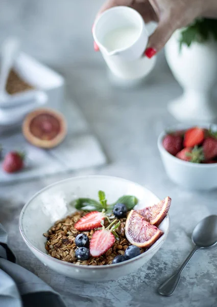 Здоровый завтрак с мюсли, йогуртом, фруктами, ягодами на белой тарелке в белой тарелке. Выборочный фокус. Женщина наливает молоко в мюсли . — стоковое фото