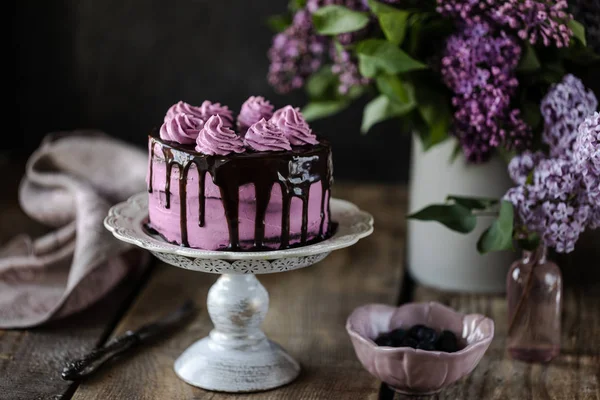 Auf dem Tisch liegt ein schöner Schokoladenkuchen und ein Strauß Flieder. dunkel — Stockfoto