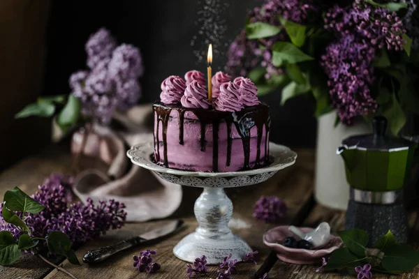 Na stole jest piękny tort czekoladowy i bukiet bzu. ciemność — Zdjęcie stockowe