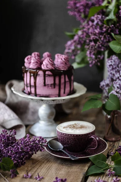 Auf dem Tisch liegt ein schöner Schokoladenkuchen und ein Strauß Flieder. dunkel — Stockfoto