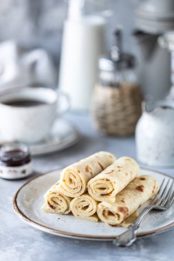Beyaz bir masada, bir fincan kahve ve bir şişe sütle bir tabağa istiflenmiş krepler.