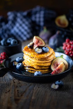 Pumpkin pancakes with syrup or honey, flax seeds, figs, blueberries in a dark plate on the table, selective focus, copy space