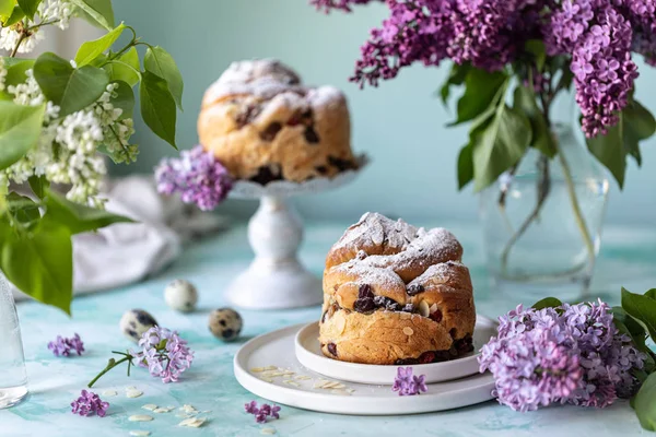 Traditioneller Cupcake Osterkuchen Kraffin mit Rosinen und Puderzucker auf dem Tisch. Osterkuchen, Kerzen und ein Strauß fliederfarbener Blumen. — Stockfoto