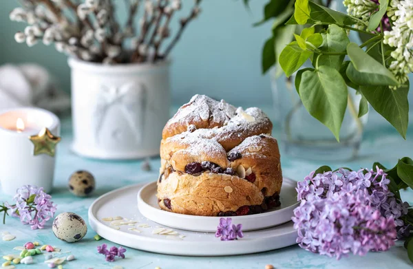 Traditioneller Cupcake Osterkuchen Kraffin mit Rosinen und Puderzucker auf dem Tisch. Osterkuchen, Kerzen und ein Strauß fliederfarbener Blumen. — Stockfoto