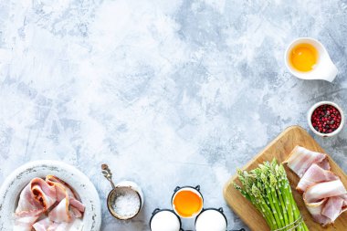 Gri beton arka planda yemek pişirmek için gerekli malzemeler. Bir demet taze kuşkonmaz, yumurta ve pastırma. Üst Manzara. Uzayı kopyala Yatay
