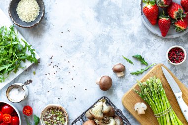 Gri beton arka planda yemek pişirmek için gerekli malzemeler. Bir demet taze kuşkonmaz, çilek, mantar, domates, roka. Üst Manzara. Uzayı kopyala Yatay