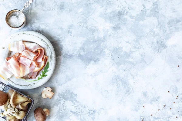 Gri beton arka planda yemek pişirmek için gerekli malzemeler. Bir demet taze kuşkonmaz, yumurta, pastırma, mantar. Üst Manzara. Uzayı kopyala Yatay