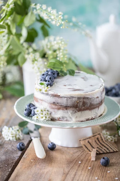 Homemade cherry cake with cream mascarpone on a light background and a bouquet of cherry flowers and lilacs. — Stock Photo, Image