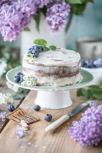 Homemade cherry cake with cream mascarpone on a light background and a bouquet of cherry flowers and lilacs. — Zdjęcie stockowe
