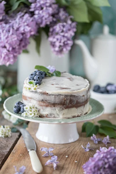 Homemade cherry cake with cream mascarpone on a light background and a bouquet of cherry flowers and lilacs. — Stockfoto