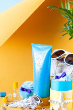 Güneş kremi şişeleri, gözlükler, sarı arka planda deniz yıldızı palmiyesi yaprakları. Yazın güzellik ve bakım.