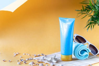 Güneş kremi şişeleri, gözlükler, sarı arka planda deniz yıldızı palmiyesi yaprakları. Yazın güzellik ve bakım.