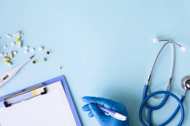 Mavi arka planda tıbbi konsept. Stetoskop, hap, tablet, not defteri, kağıt, kalem. Tıbbi maske