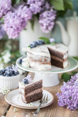 Hafif arka planda kremalı kirazlı pasta ve bir buket kiraz çiçeği ve leylak. Dikey