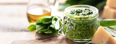 Tahta bir masada cam bir kavanozda zeytinyağı ve parmesan peynirli yaban pırasası pesto. Ramson 'ın kullanışlı özellikleri. Taze Ramson yaprakları. Pankart