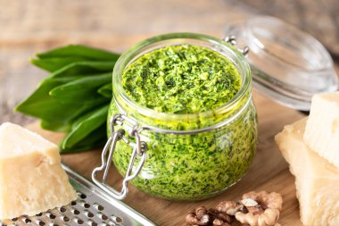 Tahta bir masada cam bir kavanozda zeytinyağı ve parmesan peynirli yaban pırasası pesto. Ramson 'ın kullanışlı özellikleri. Taze Ramson yaprakları