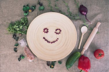 Fasulye ve taze sebzeden yapılmış gülen yüzlü tabak ve kumaş arka planda kuru yapraklar, üst manzara. 