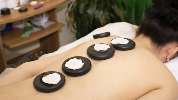 Mladá žena si hot rock masáž v salonu wellness jako vytápěné čedičové kameny jsou umístěny na její svaly před zahájením masáž — Stock fotografie