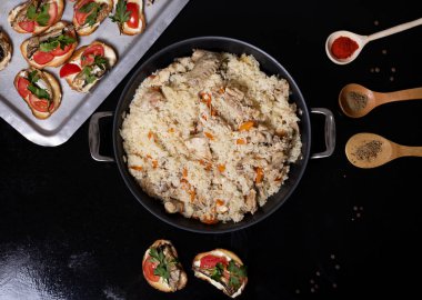 Wok with traditional spicy food called pilaf, on black background. Cooked with fried lamb, rice, garlic, carrot and raisins.