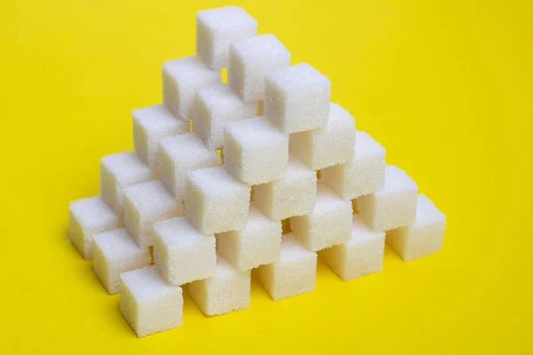 Sugar cubes pyramid on a yellow background, creative food idea