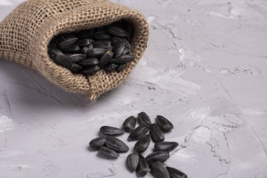 Çuvaldaki ayçiçeği tohumları, gri arka plan, seçici odak. Çuval bezinden saçılan siyah tohumlar, sıfır atık