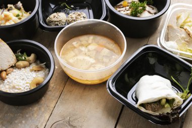 Plastik kaplarda nefis bir öğle yemeği, ahşap masada yakın çekim, sokak yemeği teslimatı.