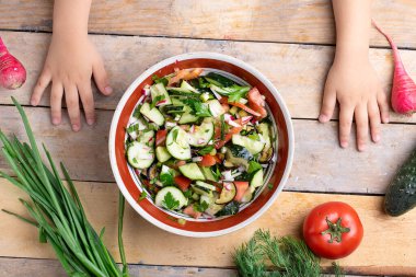 İnsan eli taze sağlıklı salatanın yanında çeşitli sebzelerin yanında, rengarenk salata kırsal ahşap masada. Çocuklar ellerini üstten görüyor