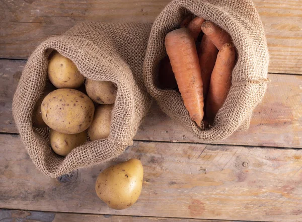 Tahta bir masanın üstünde patates ve havuç, üst manzara. Sıfır atık