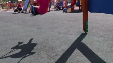 Çocuklar çocuk parkında, kız parkta sallanıyor. Çocuklu aileler dinleniyor.