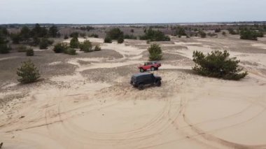 AERİAL. Siyah ve kırmızı SUV 'lar kumlu bir yolda gidiyor..