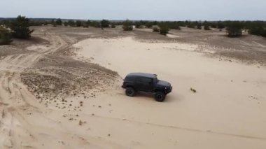  AERİAL. Siyah SUV kumlu bir yolda gidiyor. Yan görünüm.