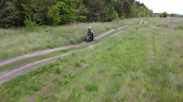 フィールドと森の間の未舗装の道路に沿って元スクーターやバイクに乗っている少女と子供 — ストック動画