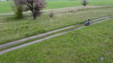 Tarlalar arasındaki toprak yolda moto scooter ya da motosiklet süren bir kız ve çocuk..